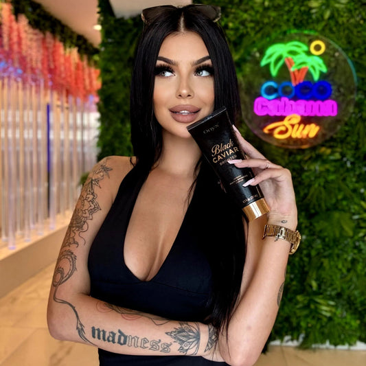 Model holding an Onyx Black Caviar Bronzer tube in front of a green feature wall in a tanning salon.