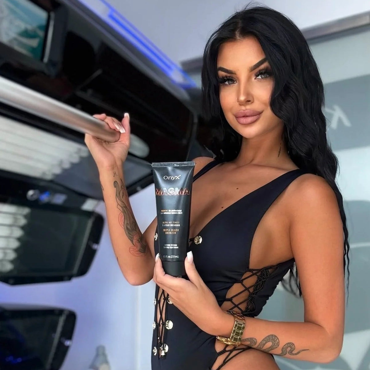 Model holding an Onyx Magma tanning lotion tube beside an open sunbed while wearing a black swimsuit.