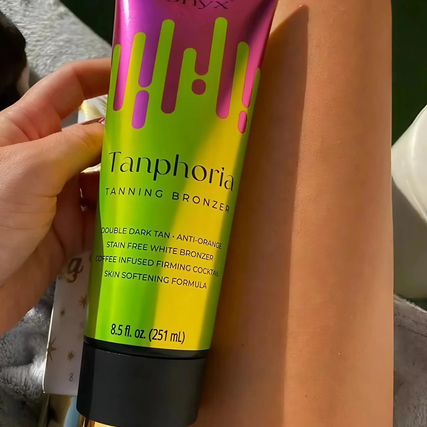 Lächelnde Frau in weißem Kleid zeigt Tanphoria Tanning Bronzer