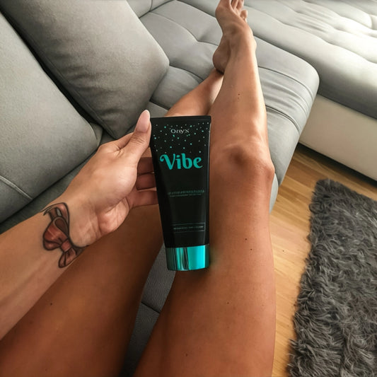 Onyx Vibe tanning accelerator cream held on tanned legs while relaxing on sofa indoors