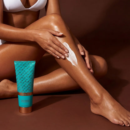 A woman applies a white tanning lotion onto her leg while the Onyx tanning accelerator tube stands nearby.