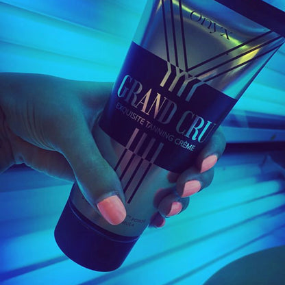 A hand holds a tube of Onyx Grand Cru Tanning Accelerator inside a glowing blue-lit tanning bed, highlighting the sleek packaging.