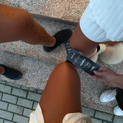 Three people with tanned legs standing on stone steps while one person holds Onyx Magma tingle tanning cream tube
