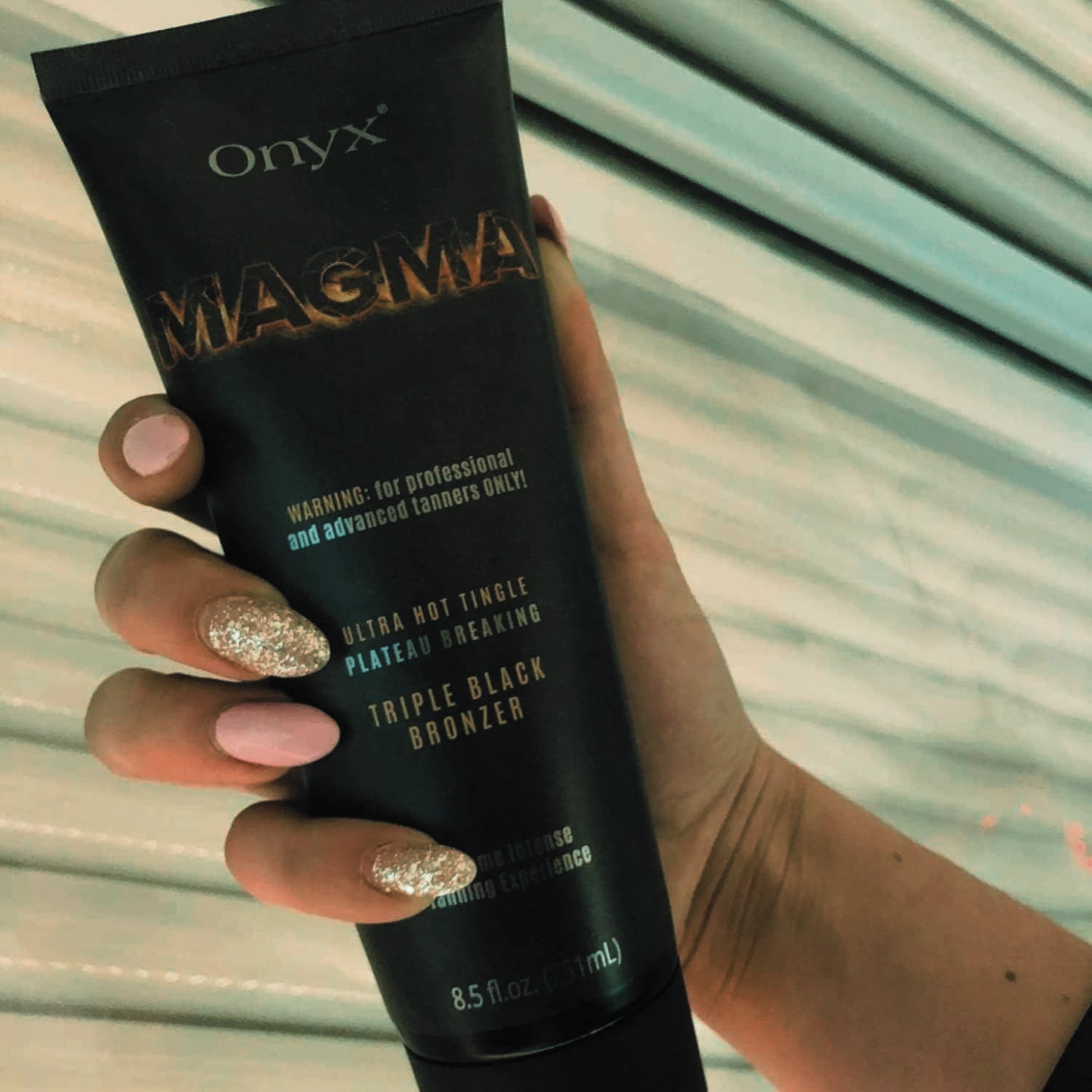 Woman with glitter manicure holding Onyx Magma tingle tanning cream near tanning bed silver panels