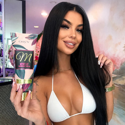 Model holding an Onyx Mystery Tanning Intensifier cream indoors while wearing a white bikini.