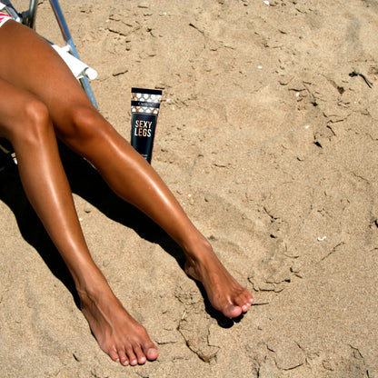 Woman’s bronzed legs stretched out on the beach with sand around and the Onyx Sexy Legs cream beside her