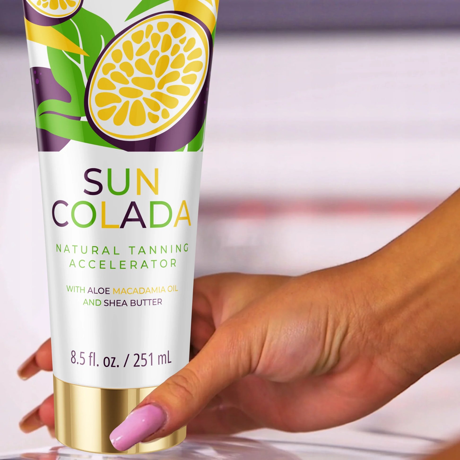 Close-up of a tanned hand holding a tube of Onyx Suncolada Accelerator sunbed cream, showing the bright tropical packaging with shea butter and macadamia oil for smooth glowing skin.