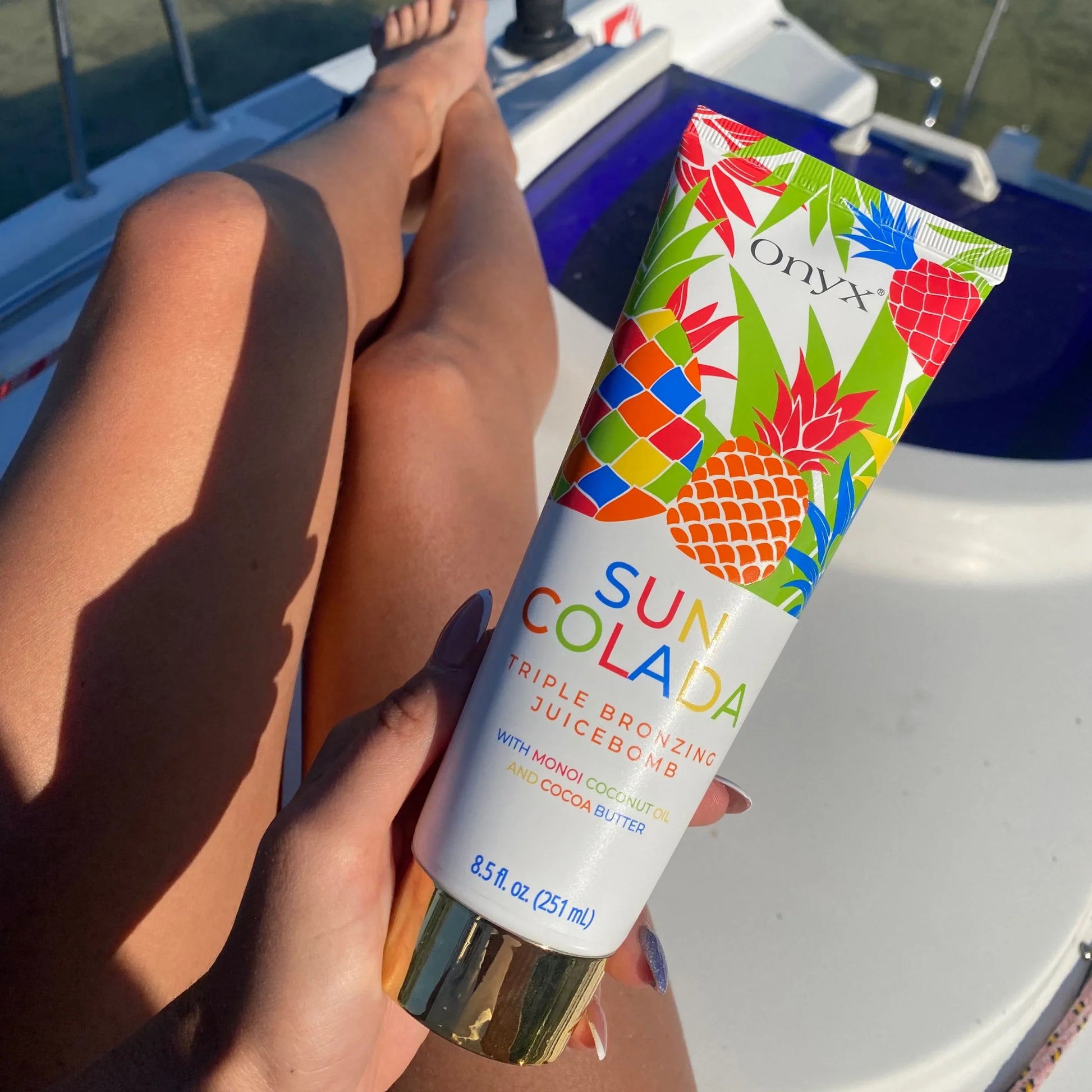 Onyx Suncolada sunbed accelerator cream displayed on tanned legs in sunlight on yacht