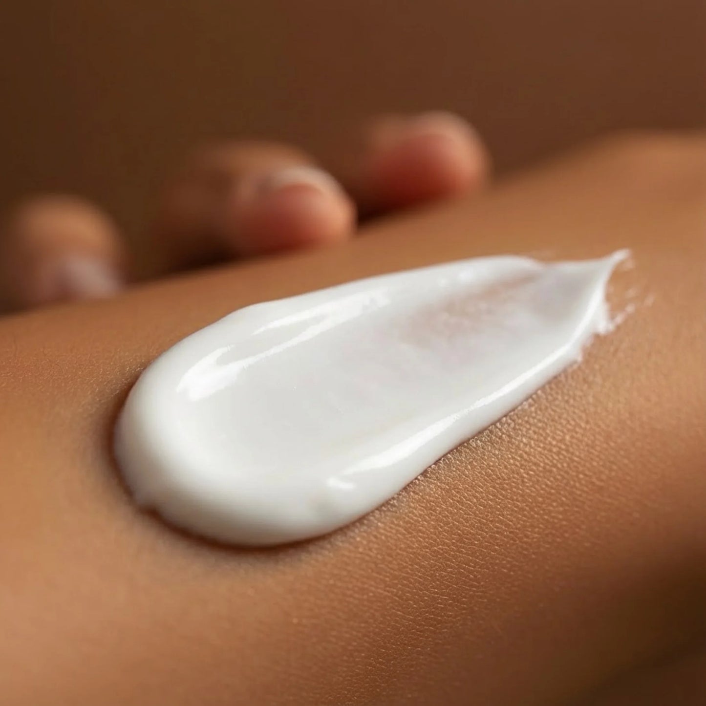 A close-up of a white tanning lotion being applied smoothly onto skin, showing its creamy texture.